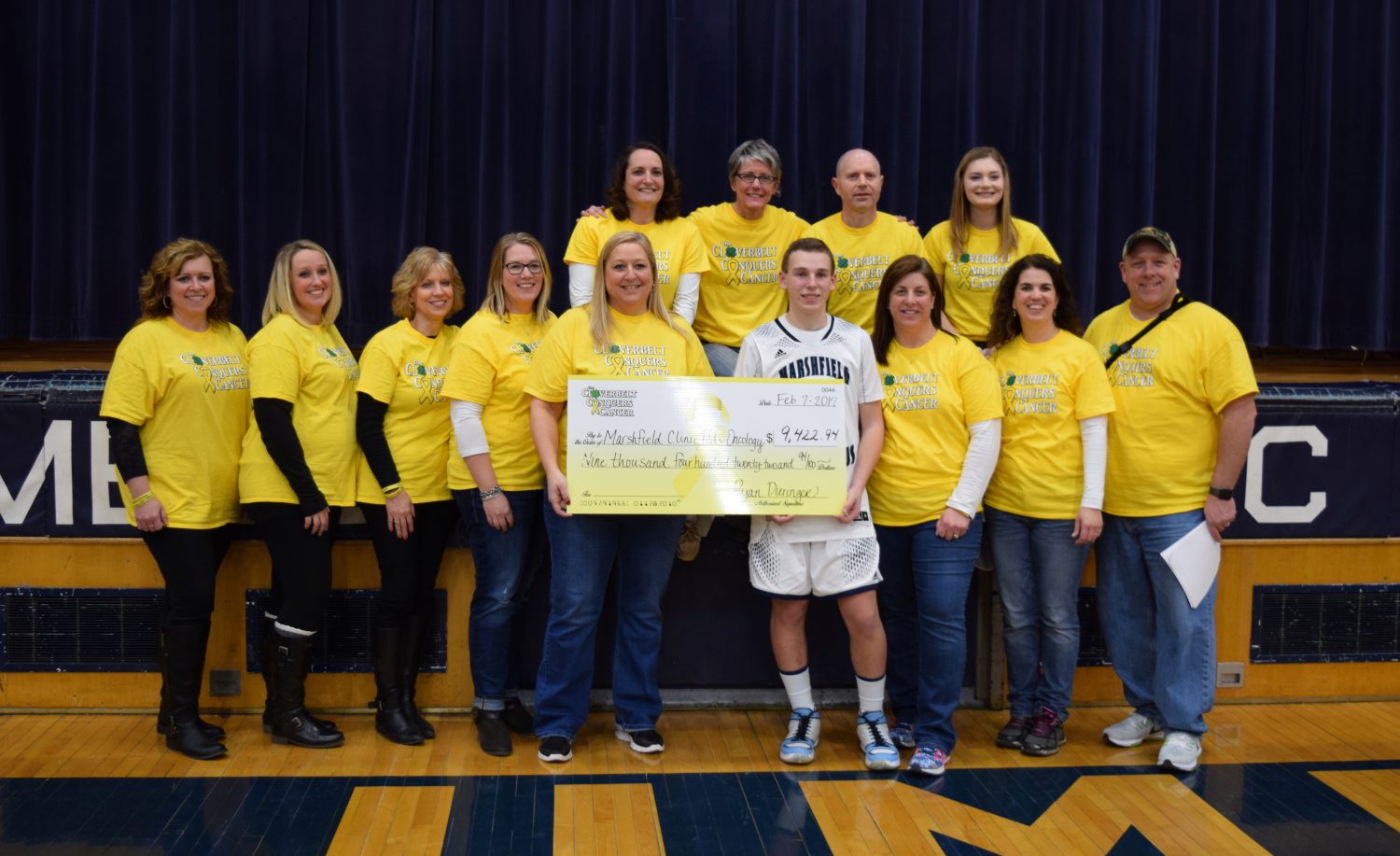 Marshfield Columbus Catholic basketball’s Ryan Dieringer, holding check and pictured with members of the Cloverbelt Conquers Cancer committee, was instrumental in creating the fundraiser following his own battle with Ewing’s sarcoma.