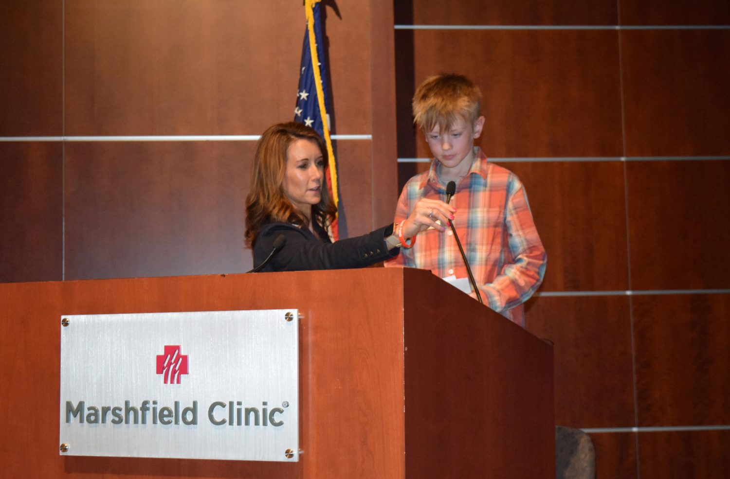 Nine-year-old cancer survivor Will Krause prepares to address the crowd at the May 10 Midwest Athletes Against Childhood Cancer Inc. check presentation to Marshfield Clinic Health System. Marshfield Clinic Health System Foundation Chief Philanthropy Officer Teri Wilczek straightens his microphone.